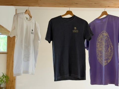 White and denim navy T-shirt fronts with embroidered chest logos, beside the violet back print