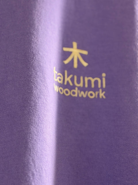Gold Takumi chest logo on violet fabric